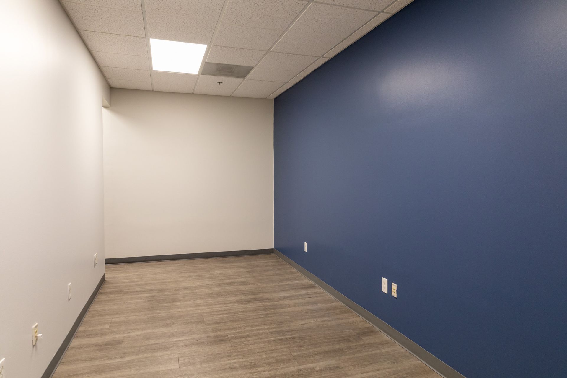 An empty room with a blue wall and a wooden floor.