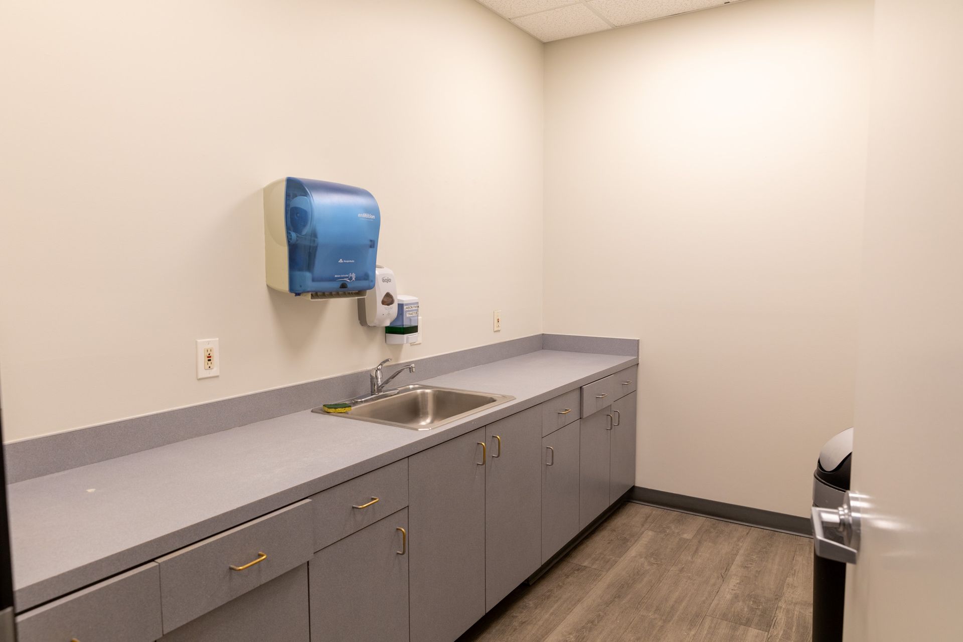 A kitchen with a sink , cabinets , drawers and a trash can.