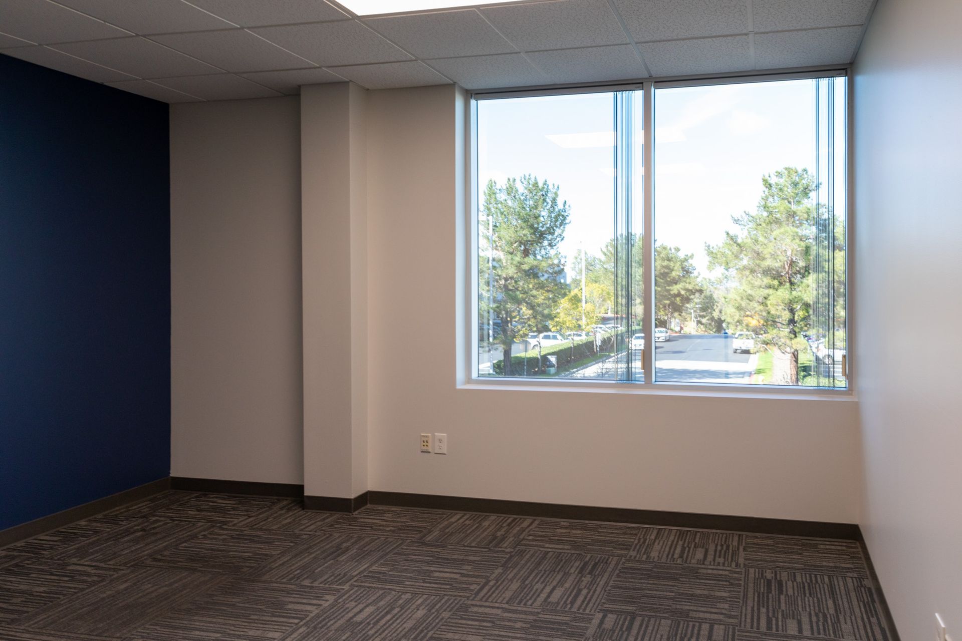 An empty room with a large window and a blue wall.
