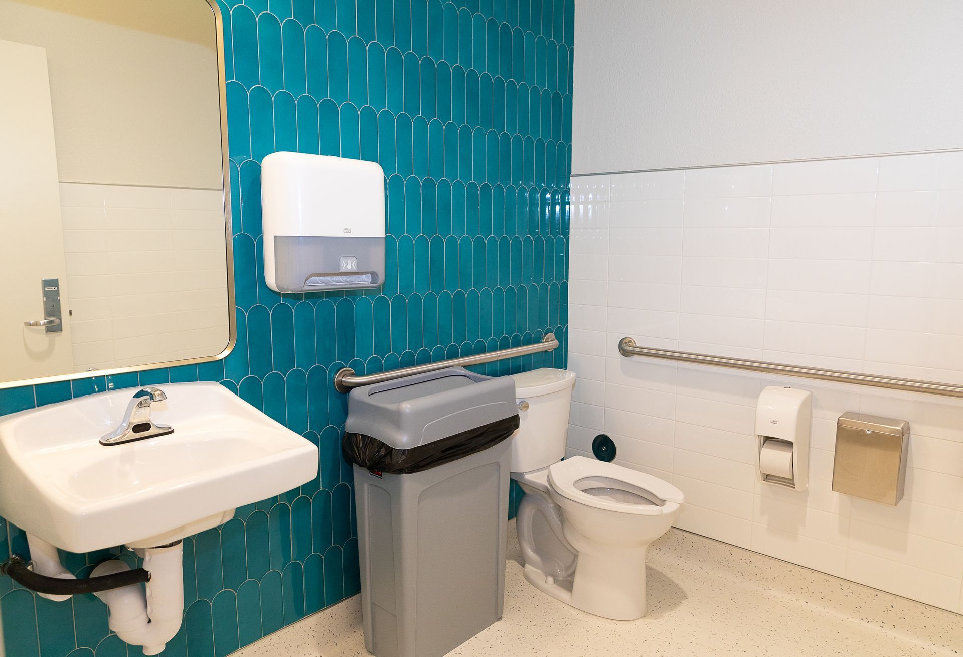 A bathroom with a sink , toilet , trash can and mirror.