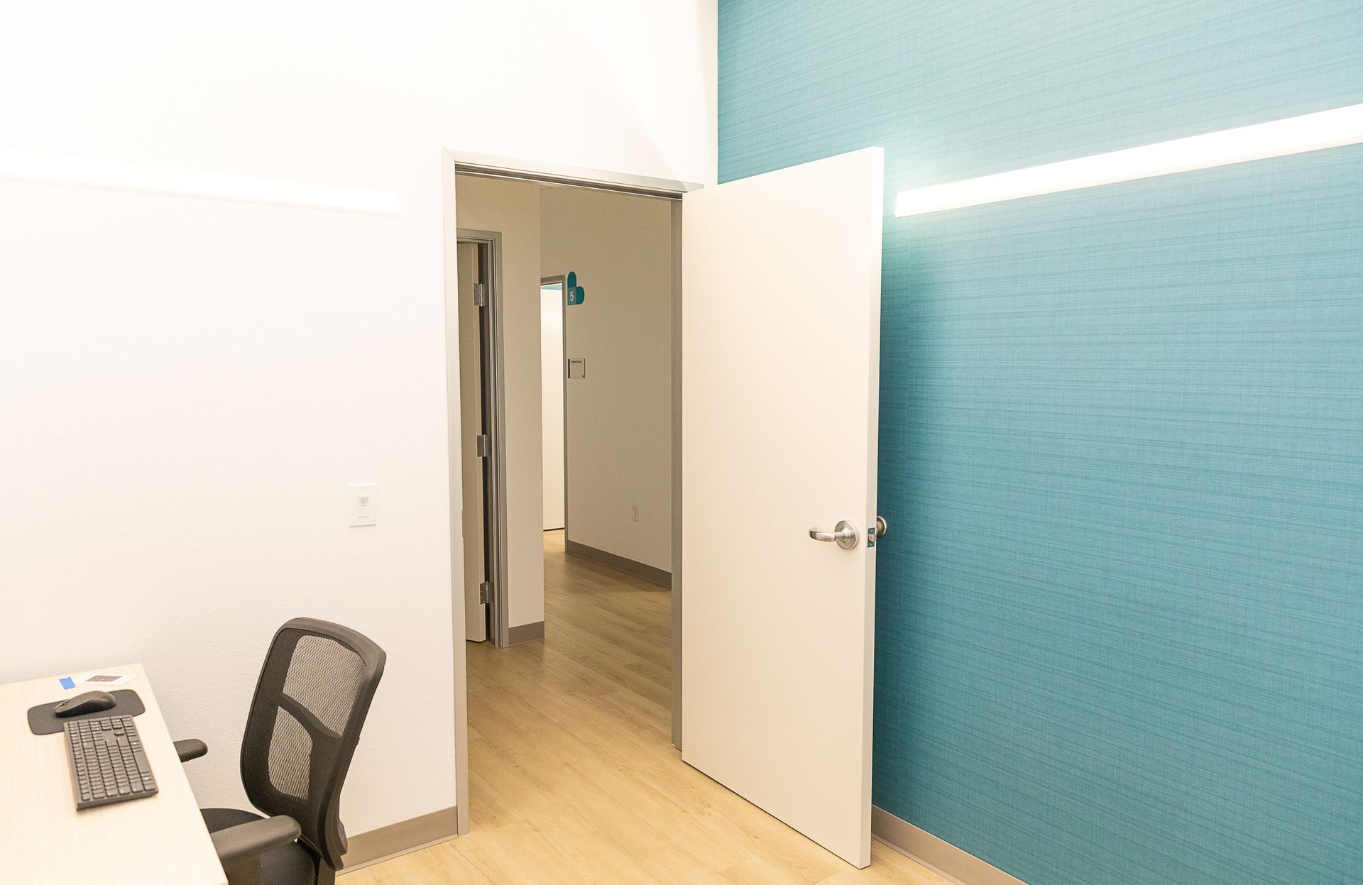 A small office with a desk and chair and a door leading to another room.