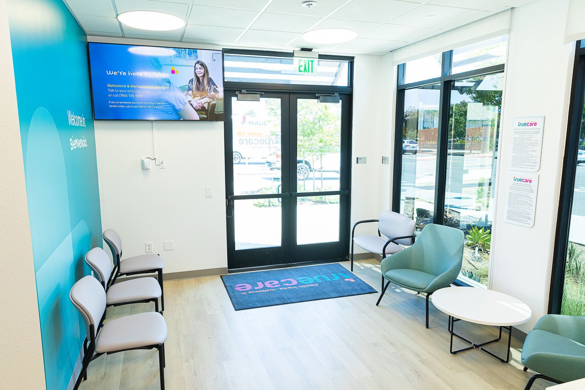 A waiting room with chairs , tables and a television on the wall.