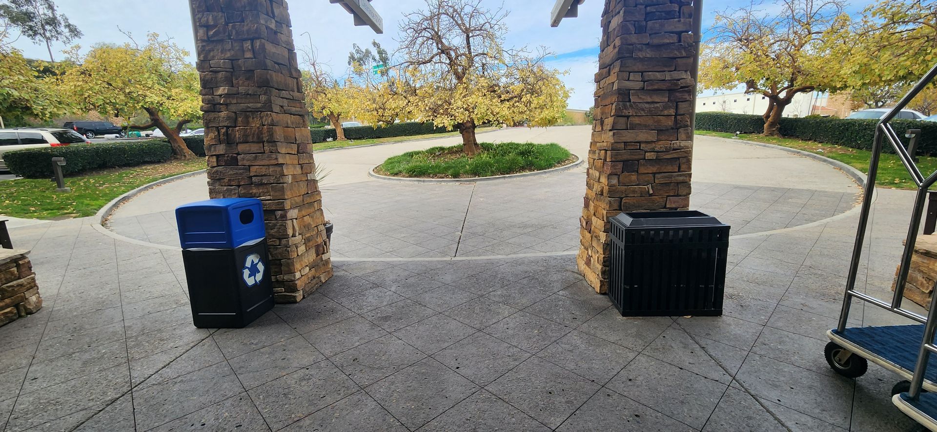 A blue trash can is sitting next to a black trash can on a sidewalk.