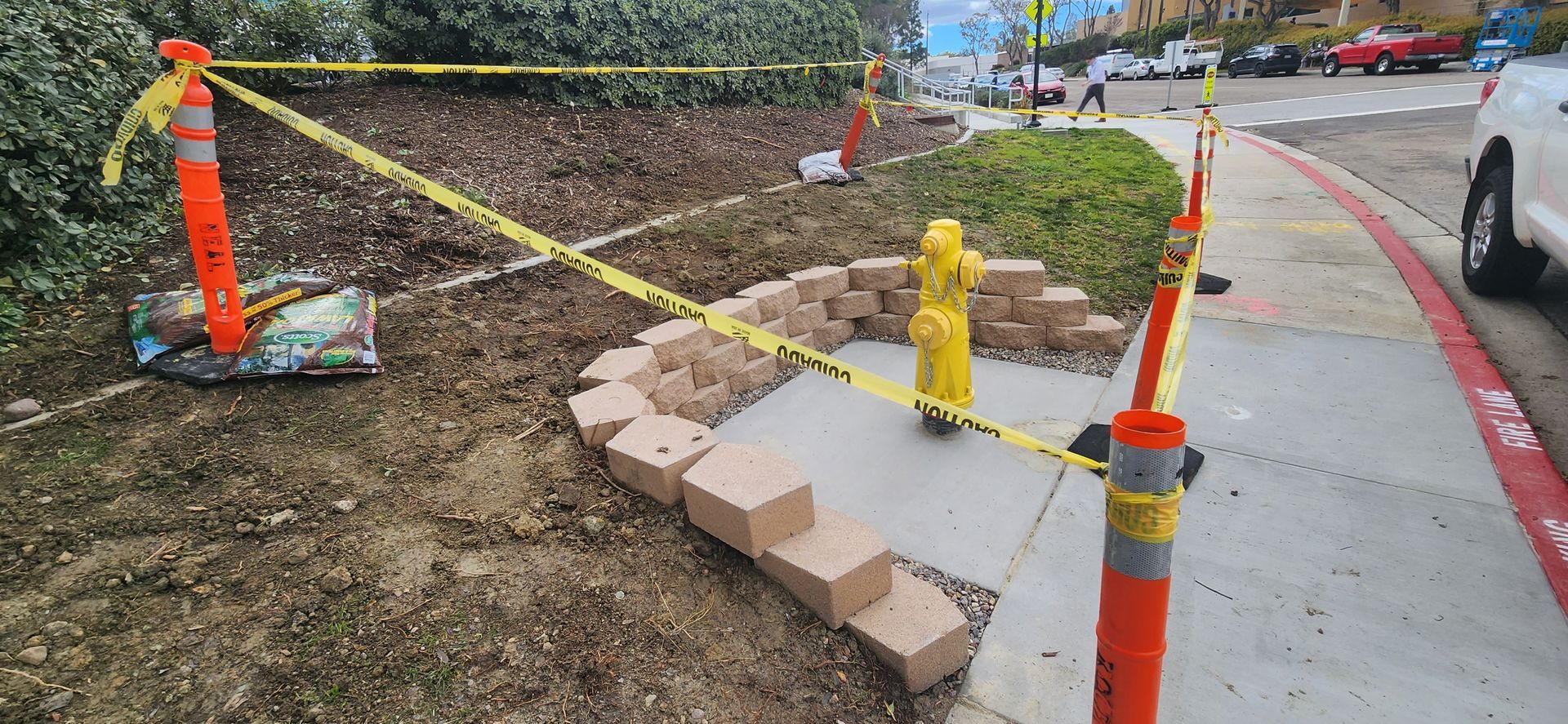 A yellow fire hydrant is sitting on a sidewalk surrounded by orange cones and yellow tape.