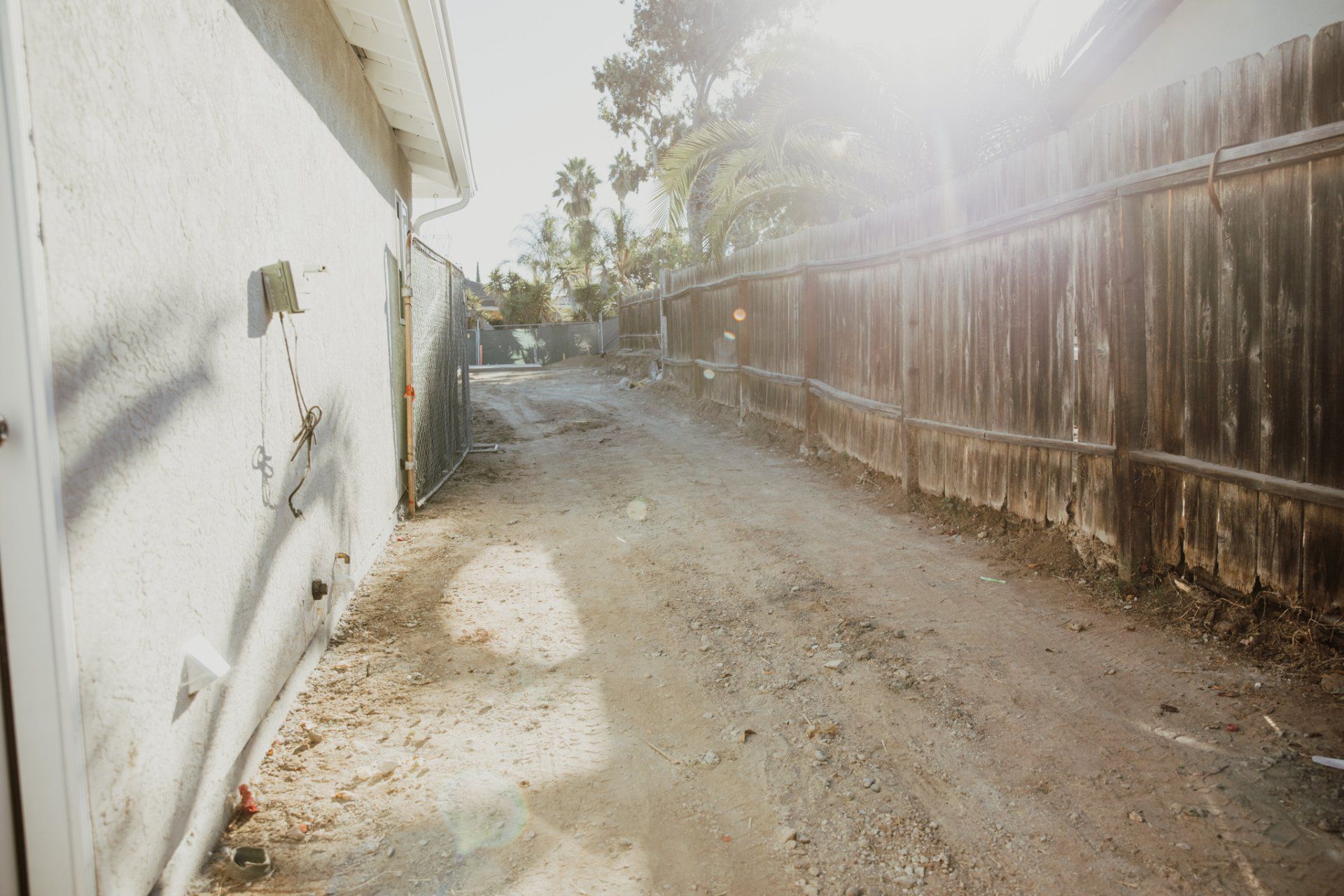 A dirt road leading to a house with a wooden fence.