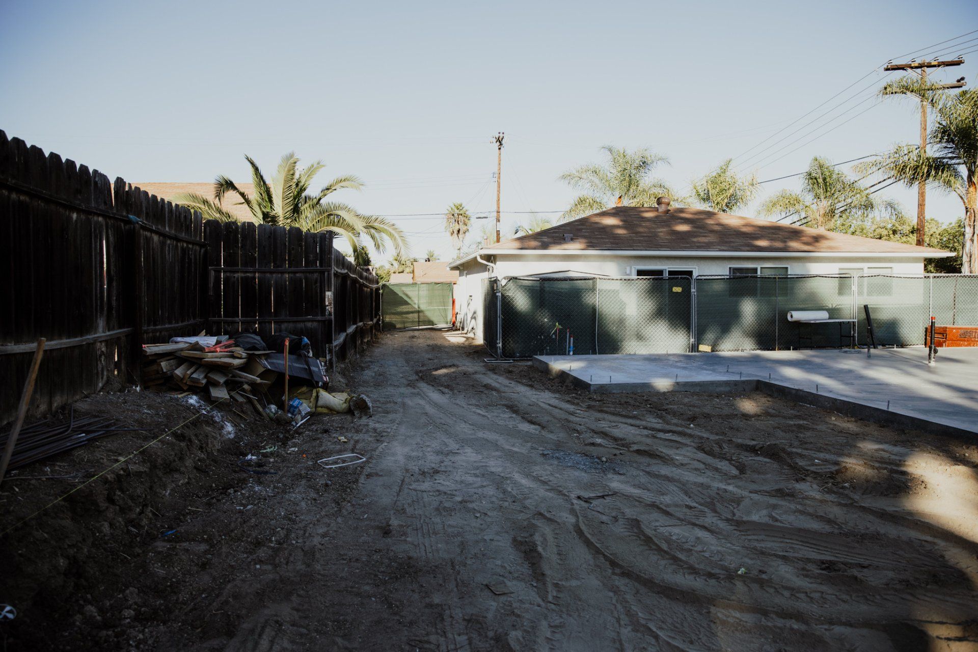 A dirt road leading to a house with a fence in the background.