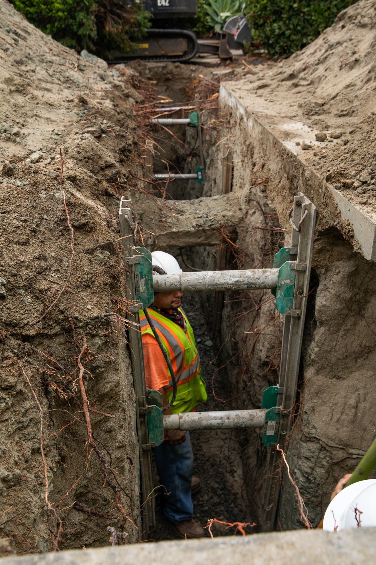 A man in a yellow vest is working in a trench