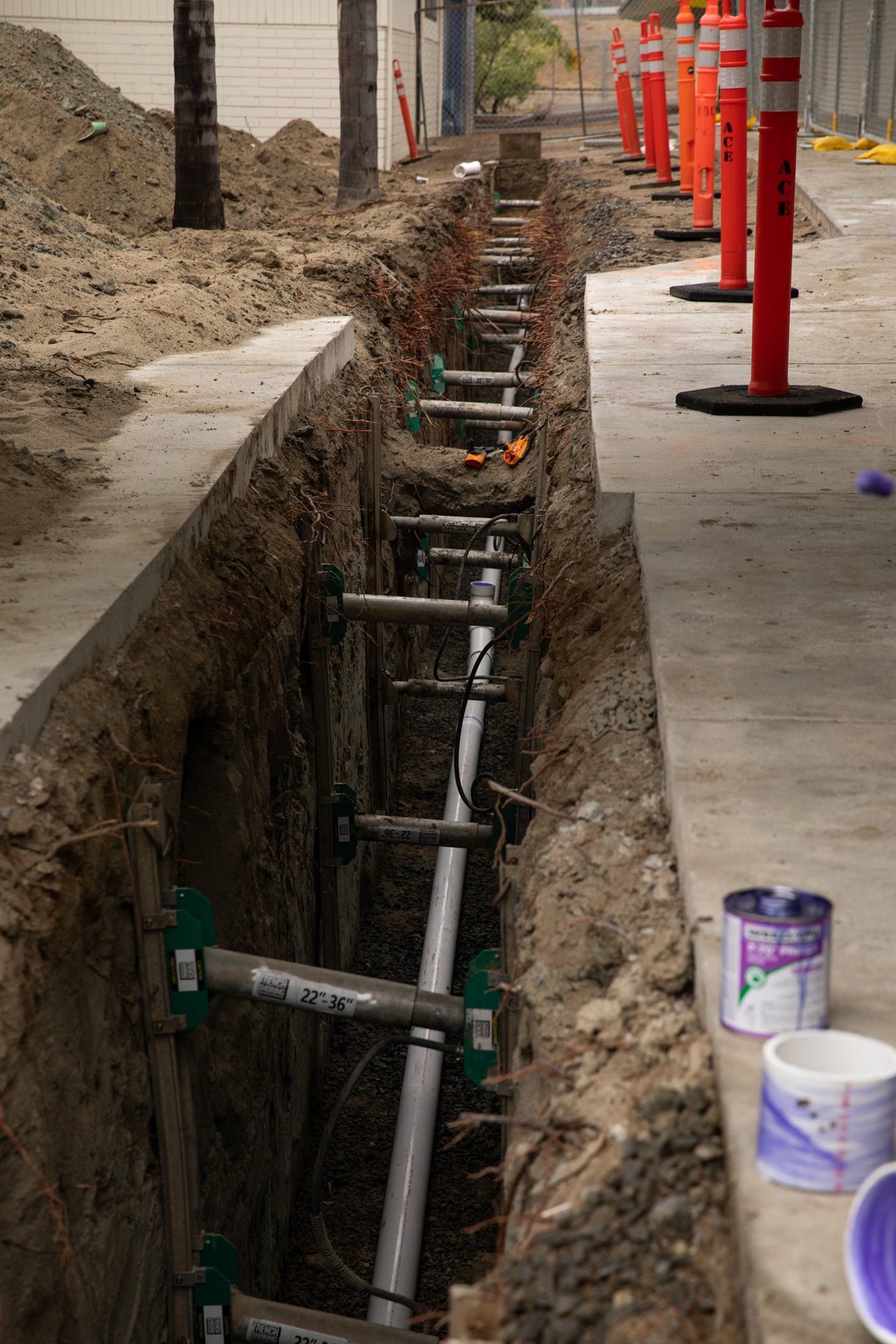 A can of purple paint sits on the sidewalk next to a trench