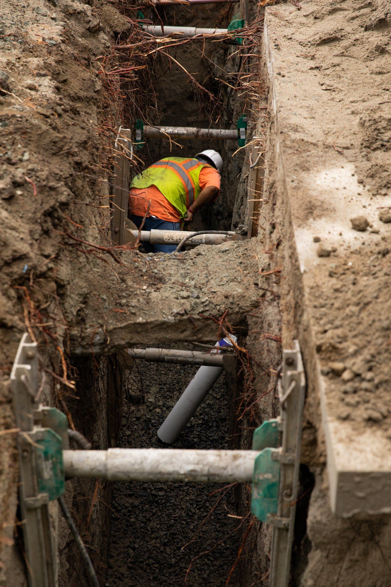 A man in a yellow vest is working in a trench
