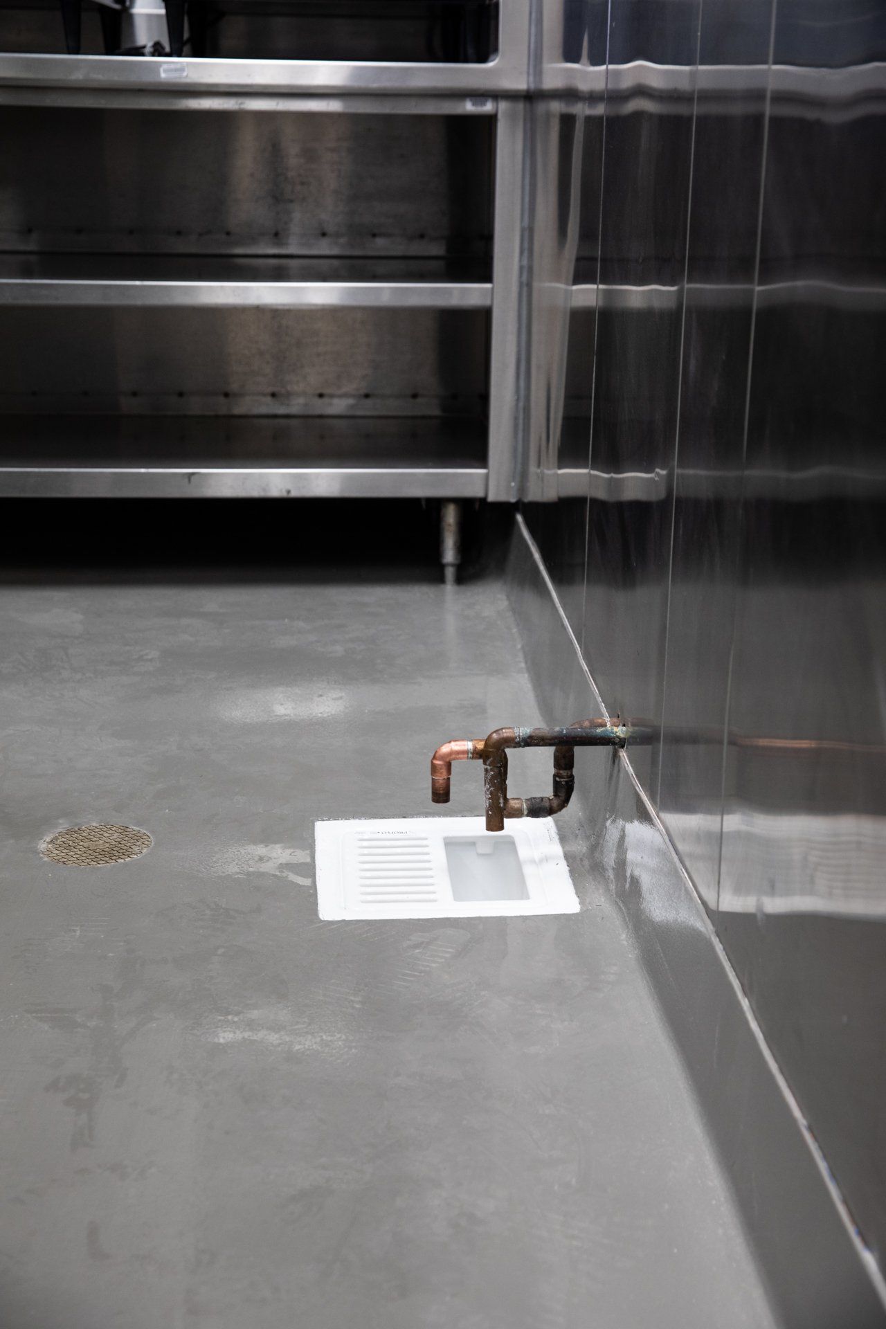 A close up of a pipe on a concrete floor in a kitchen.