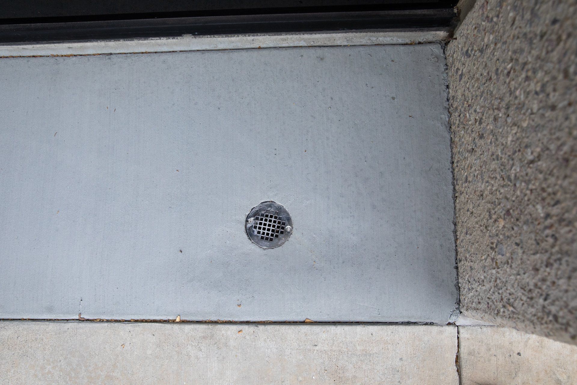 A close up of a drain on a sidewalk next to a door.