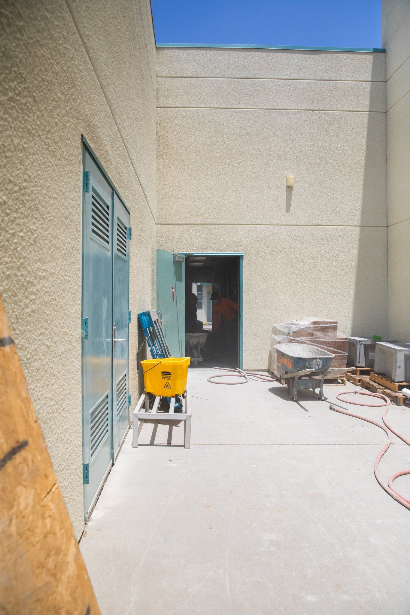 A building under construction with a yellow bucket and a wheelbarrow.