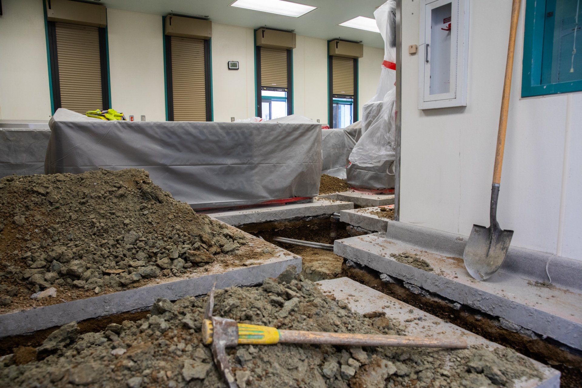 A hammer and shovel are laying on the ground in a room under construction.