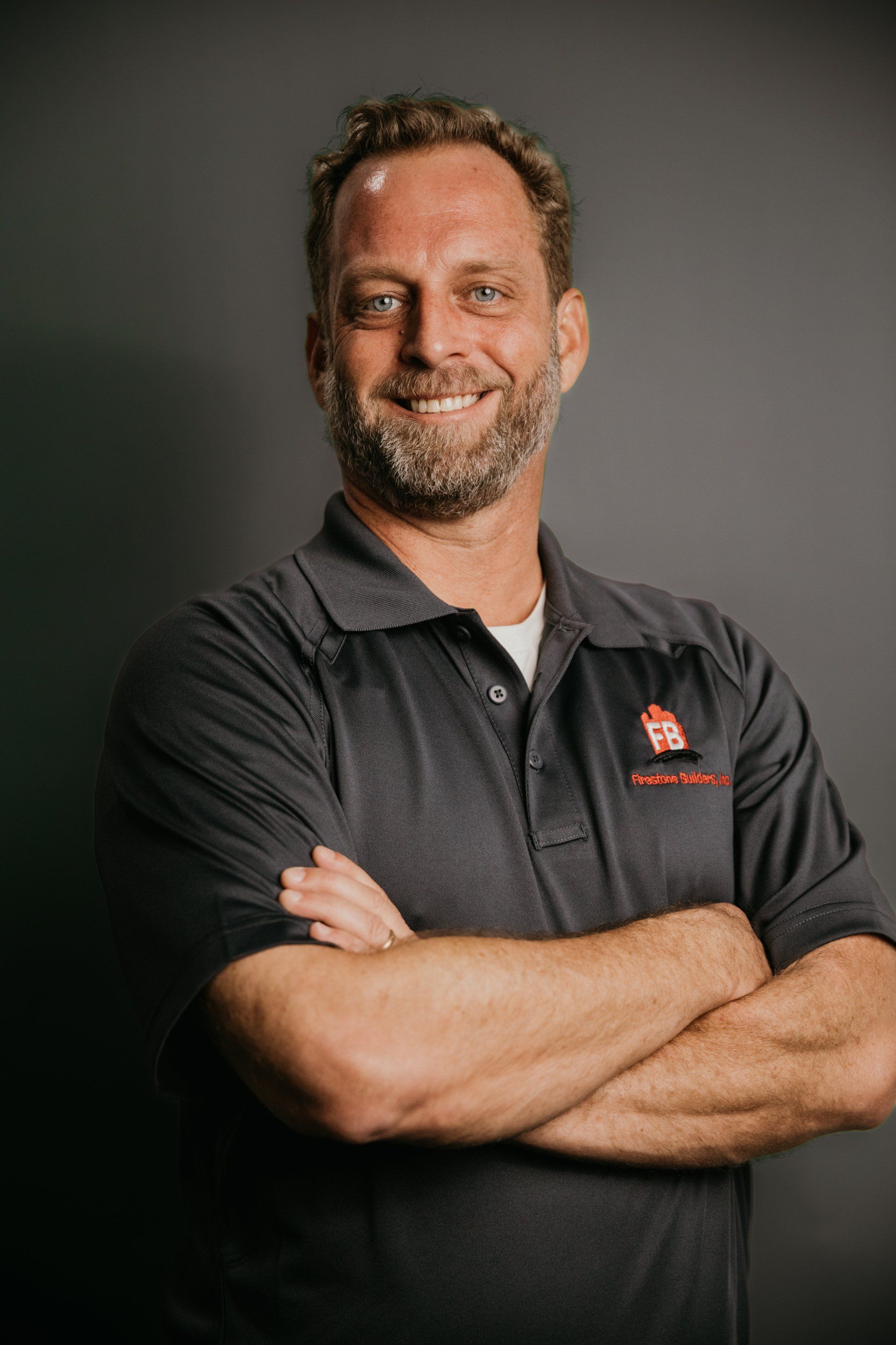 A man with a beard is standing with his arms crossed and smiling.