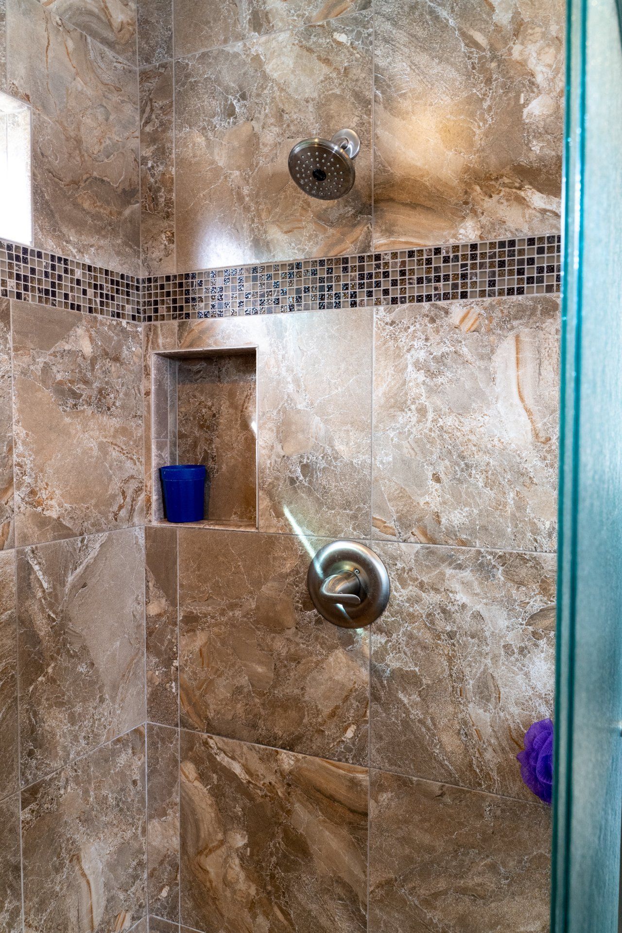 A bathroom with a shower and a blue cup on the shelf.
