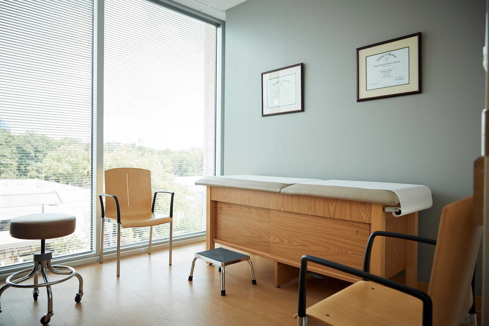 A doctor 's office with a table , chairs , and a stool.