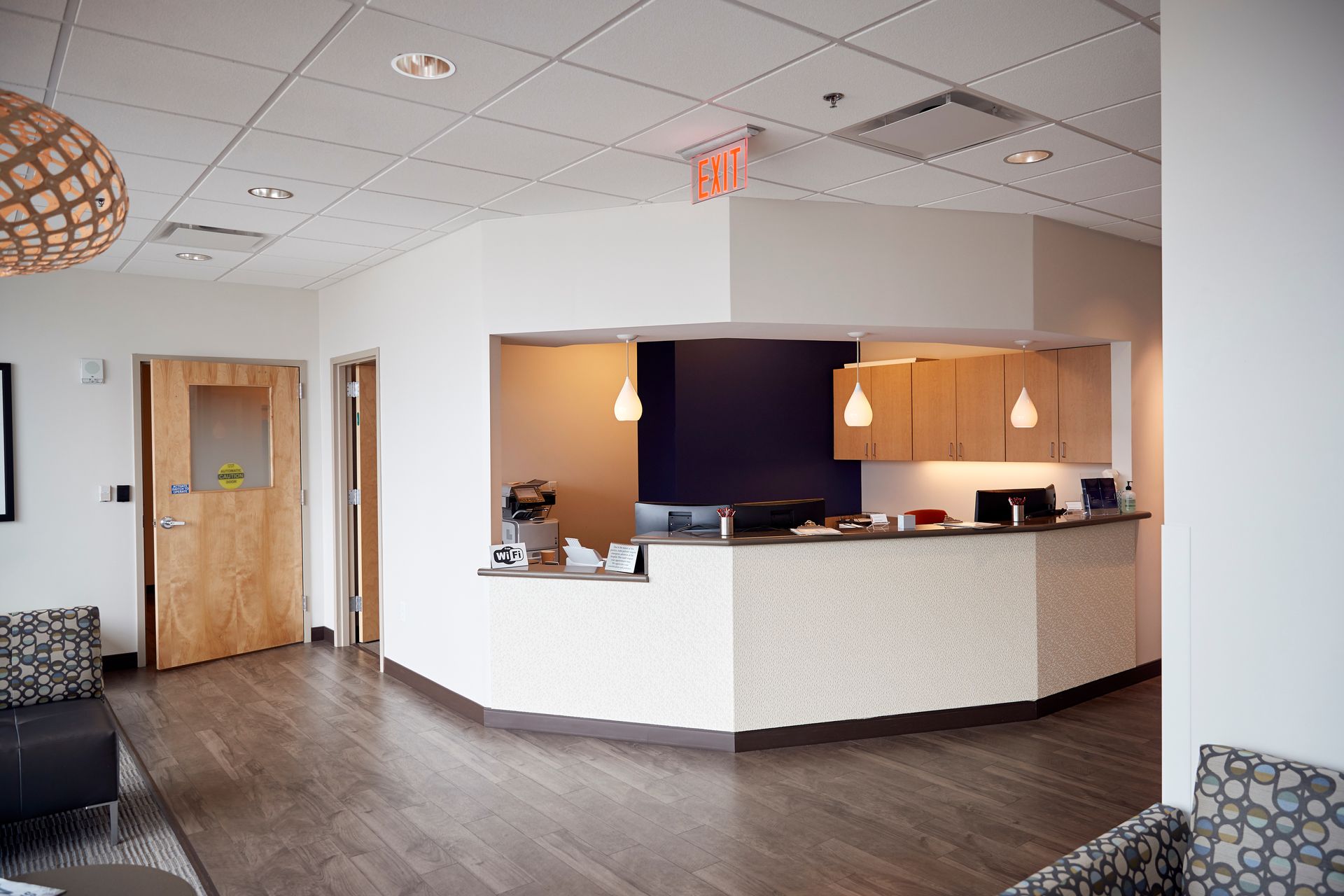 A reception area in a hospital with a red exit sign hanging from the ceiling.