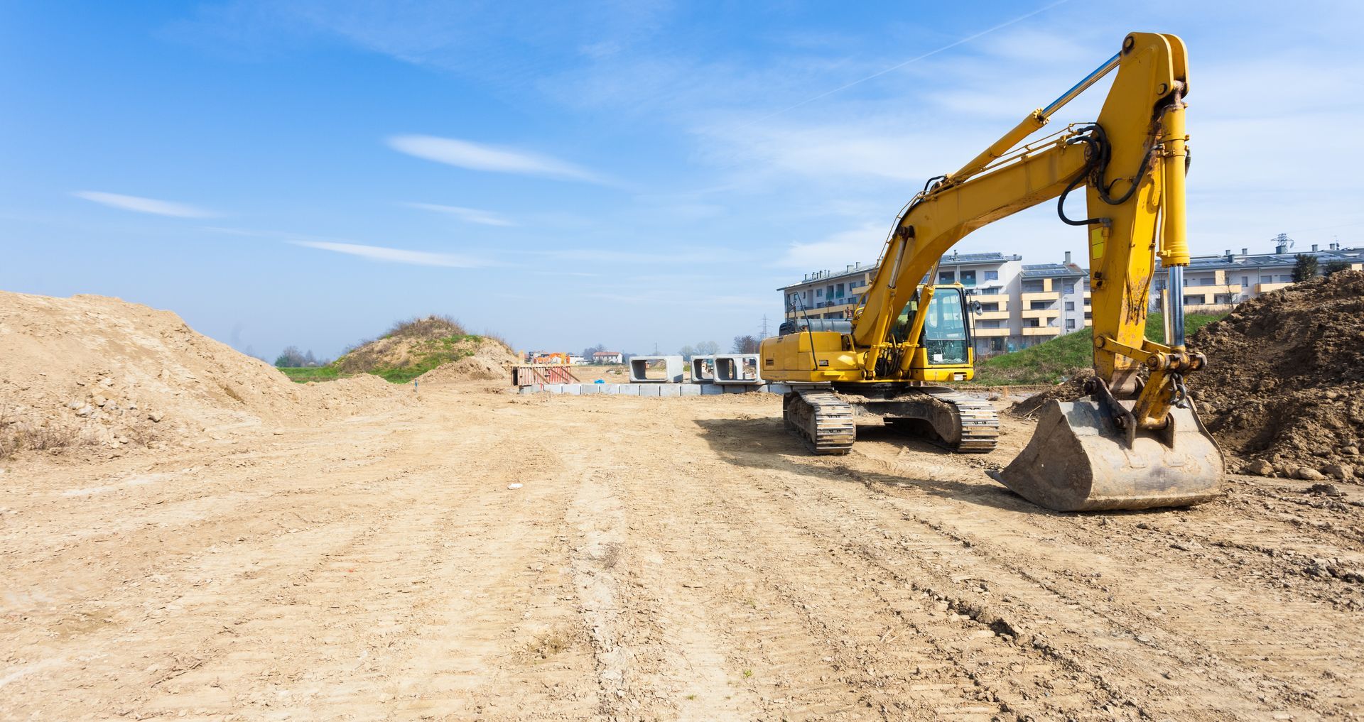 A yellow excavator is working on a dirt road at a construction site.