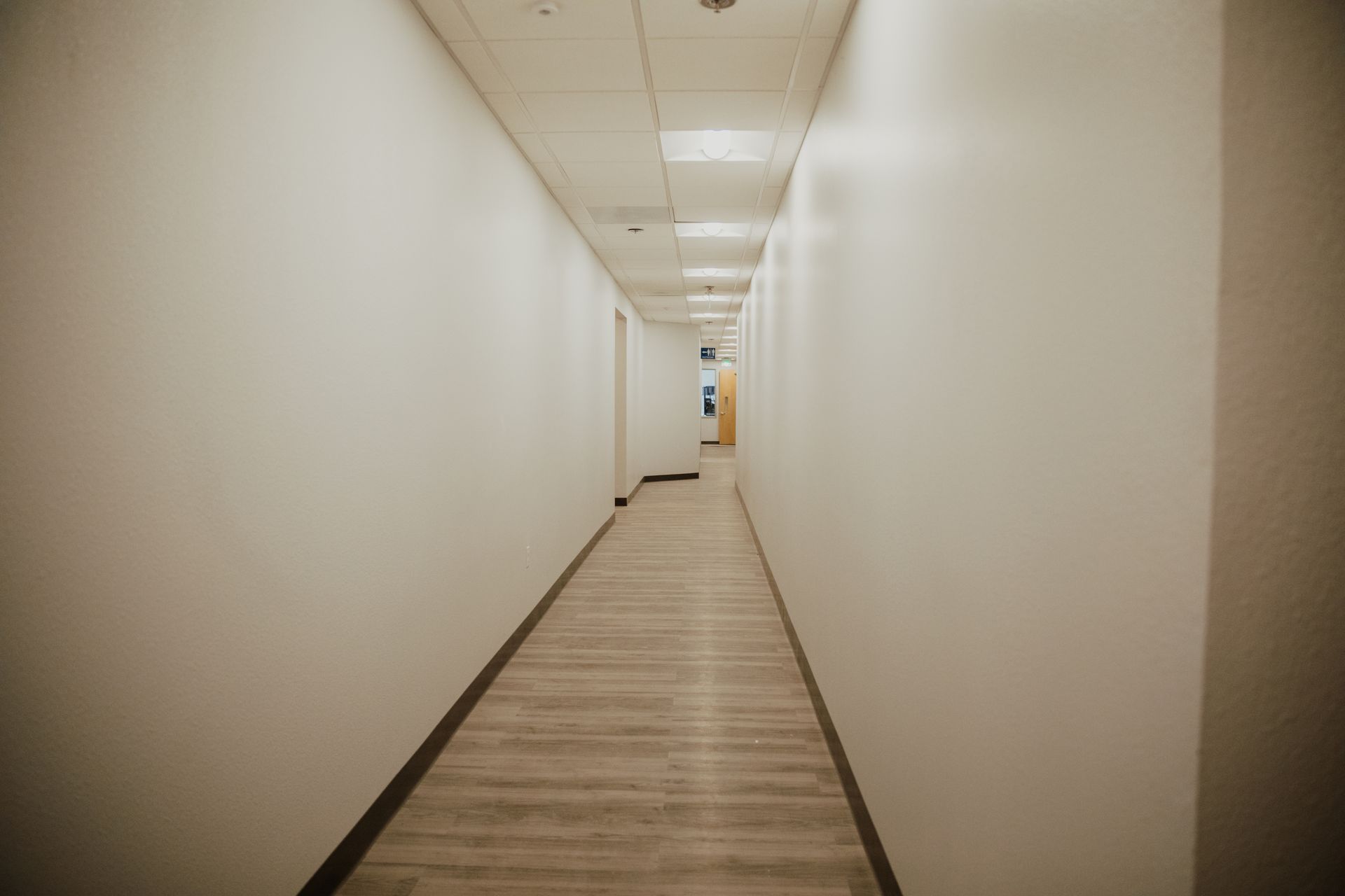An empty hallway with white walls and wooden floors in an office building.