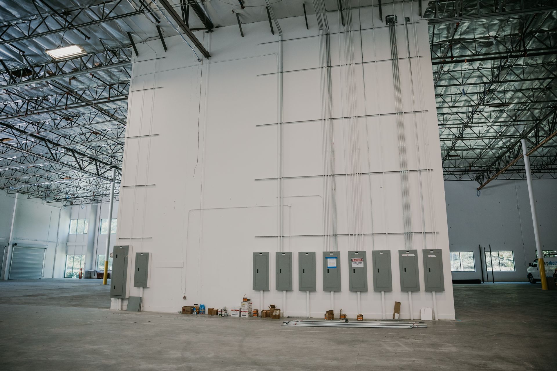 A large white wall in an empty warehouse with electrical panels on it.