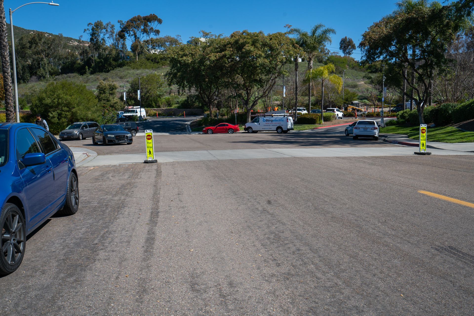 A blue car is parked on the side of the road in a parking lot.