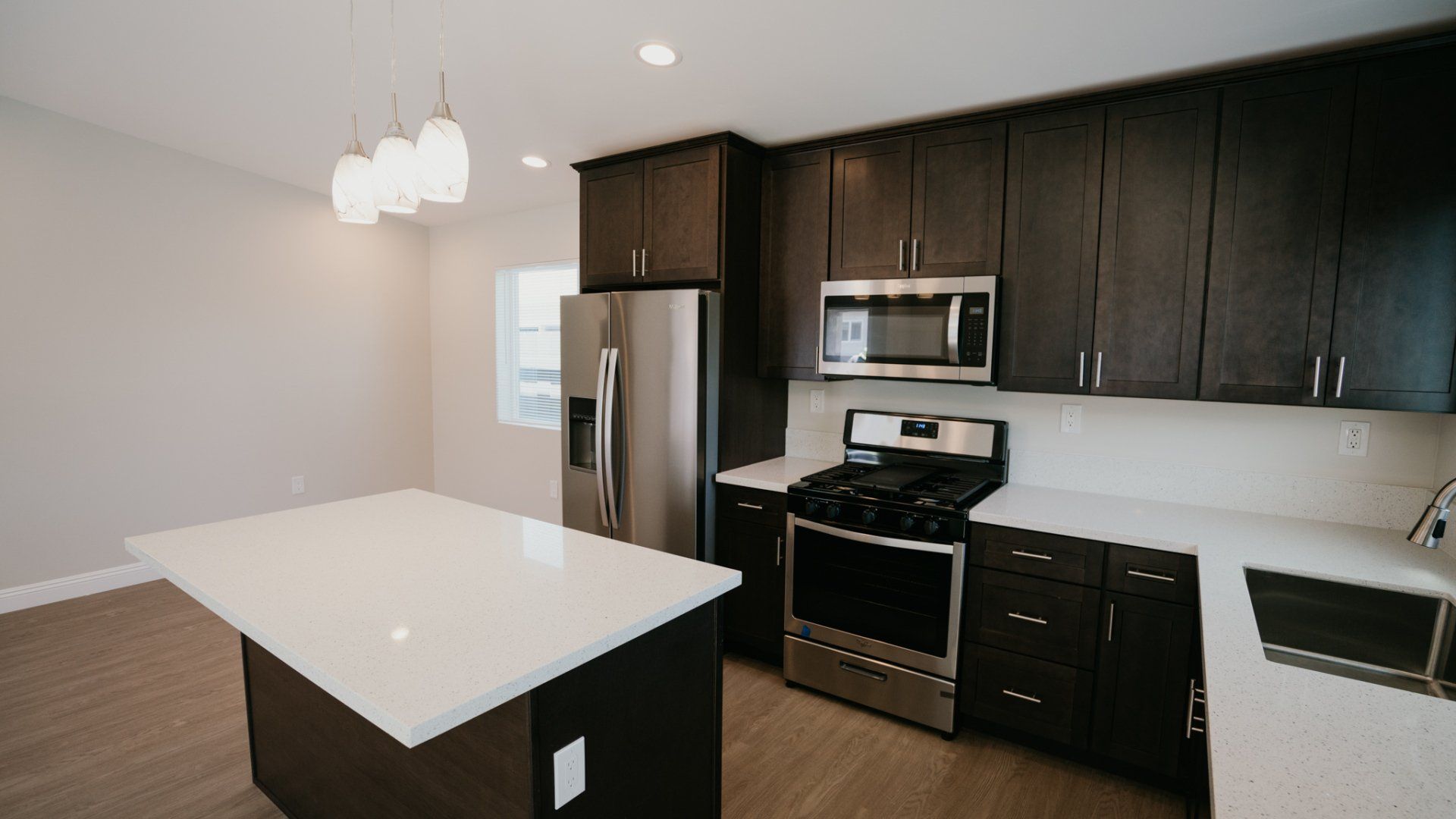 A kitchen with a stove , refrigerator , microwave and sink.