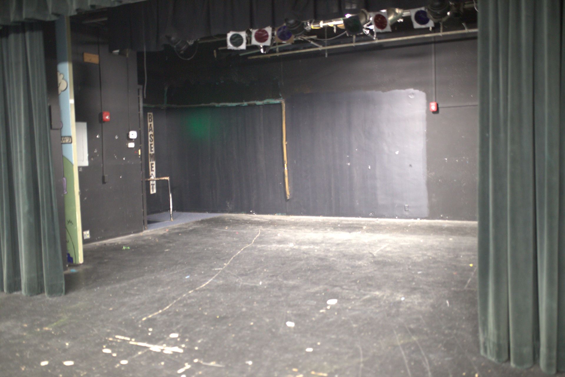 An empty stage with a green curtain and a red exit sign