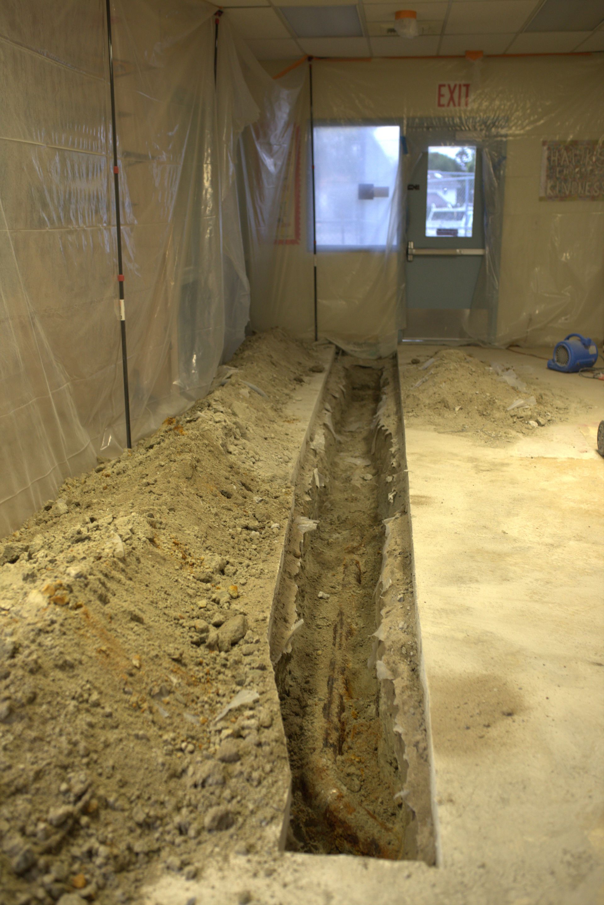 A room with a hole in the floor and an exit sign on the wall.