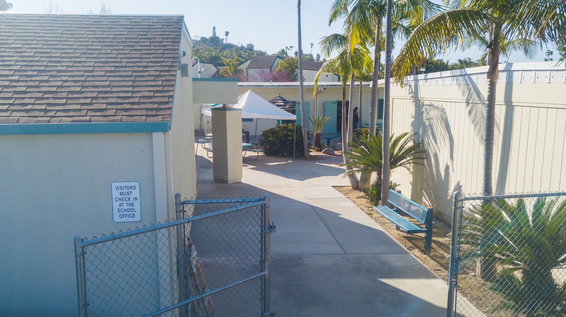 A chain link fence surrounds a concrete walkway leading to a building.