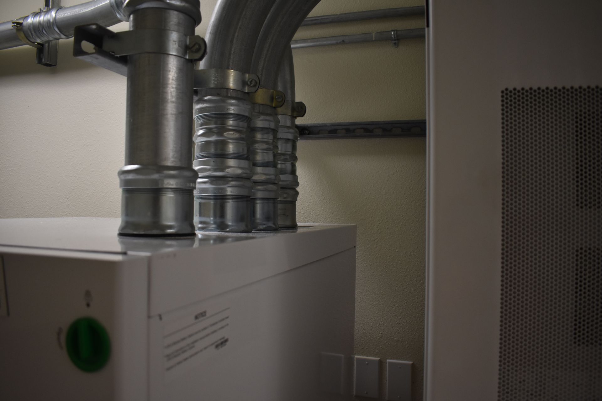A close up of a boiler with pipes coming out of it in a room.
