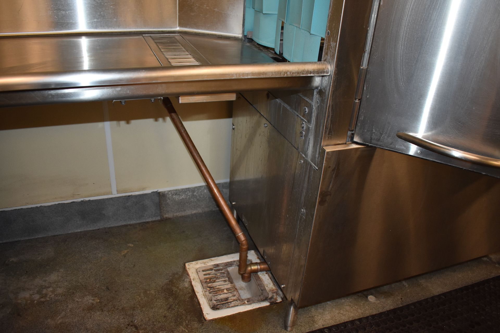 A mop is sitting under a stainless steel shelf in a kitchen.