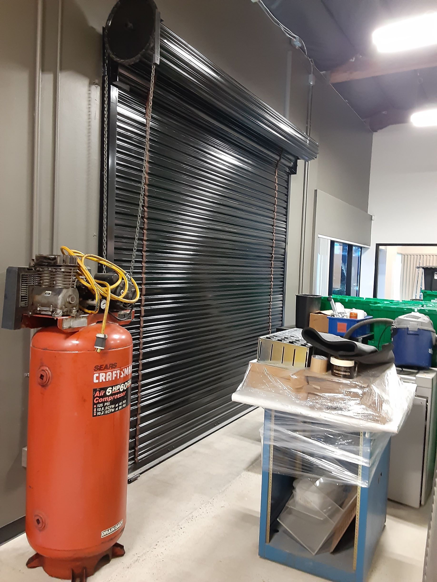 A red air compressor is sitting in front of a garage door.