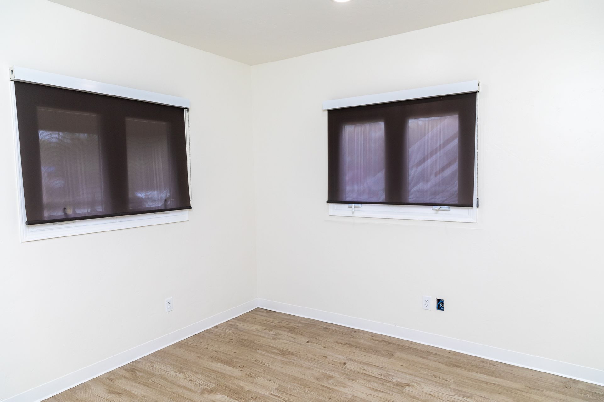 An empty room with two windows and a wooden floor.