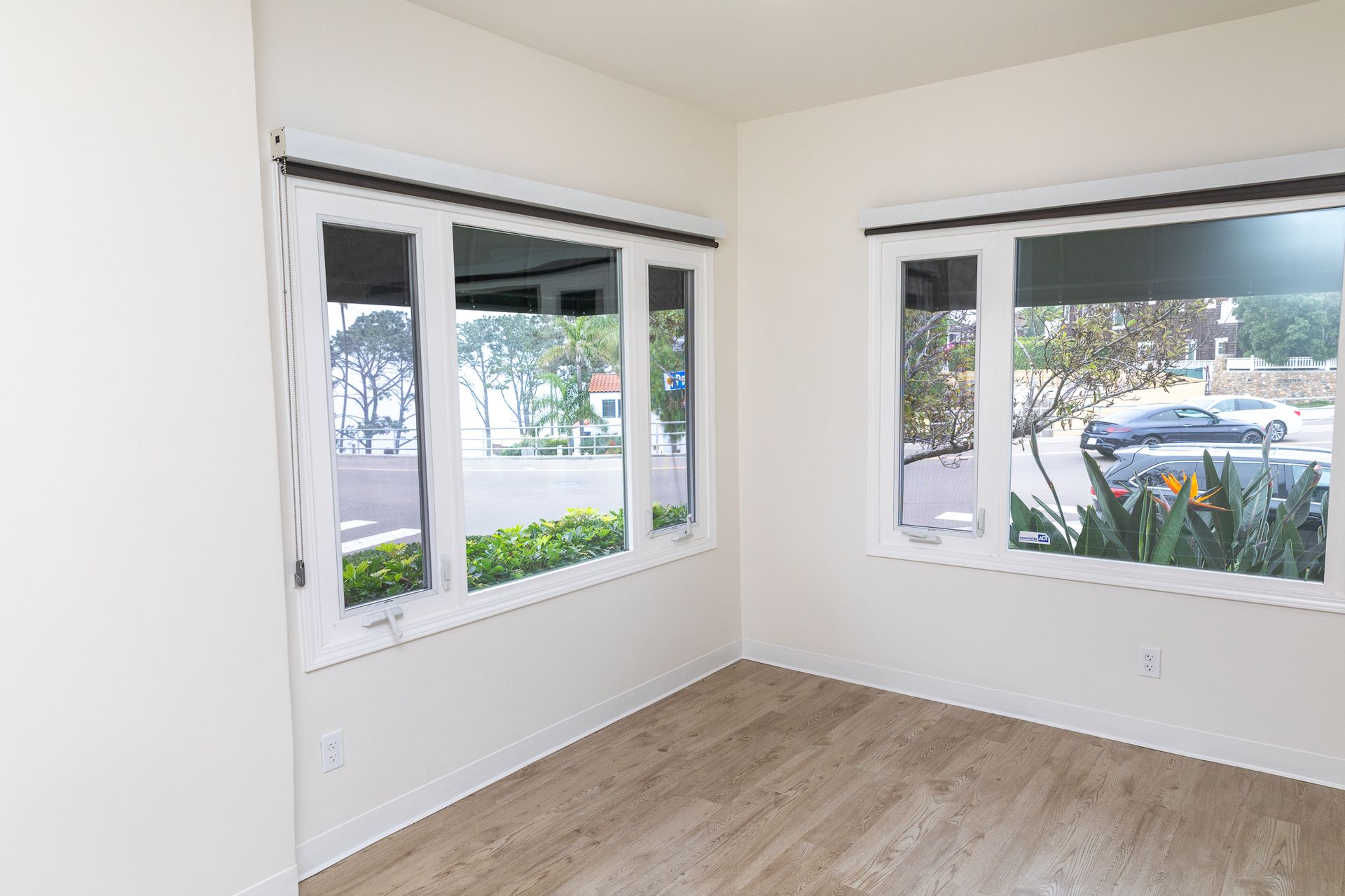 An empty room with two windows and a wooden floor.