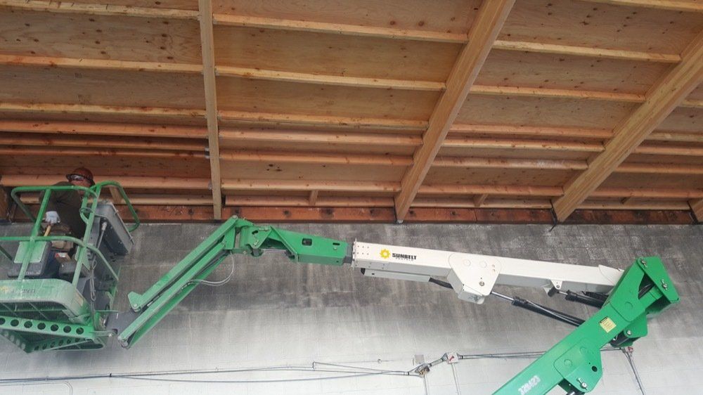 A green aerial lift is being used to lift a large piece of wood