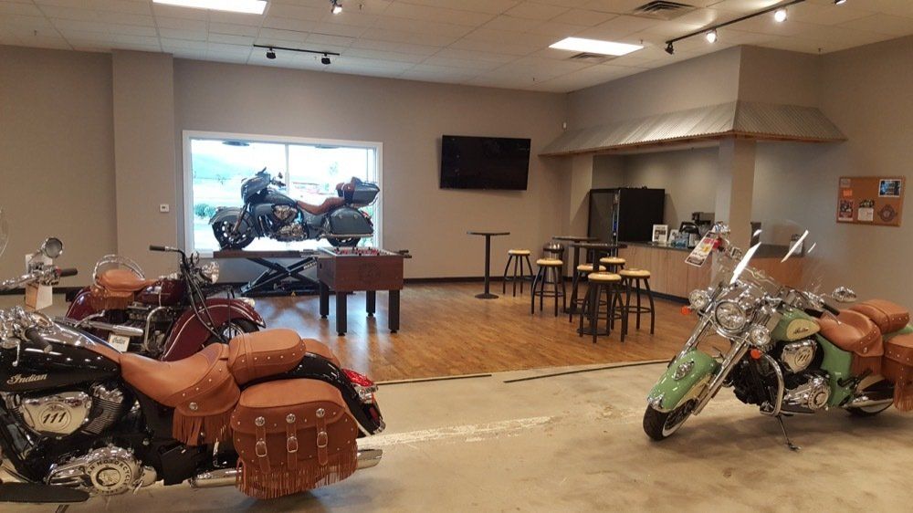 Two motorcycles are parked in a room with tables and chairs.