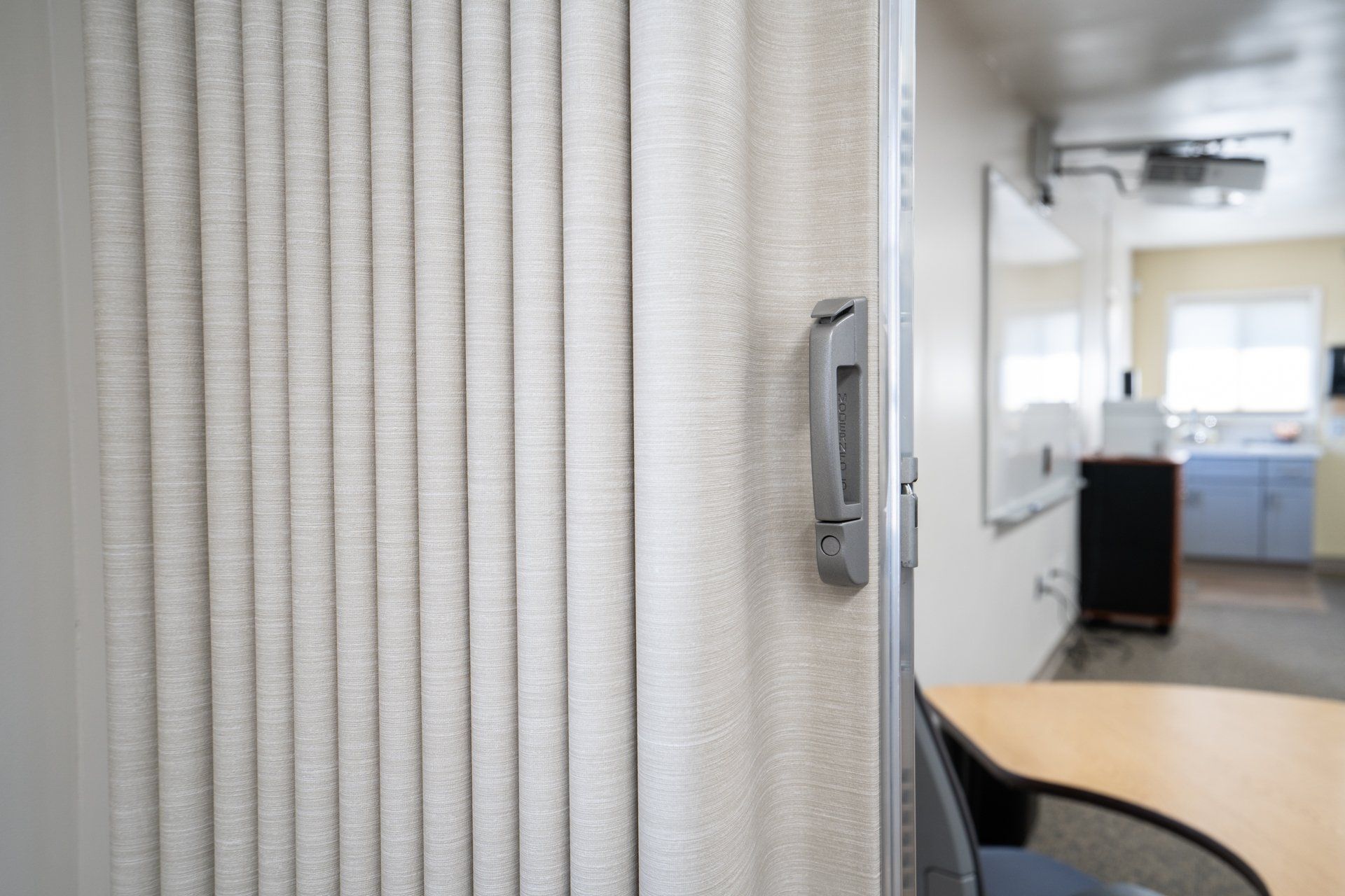 A white accordion door is open to a classroom with a table and chairs.