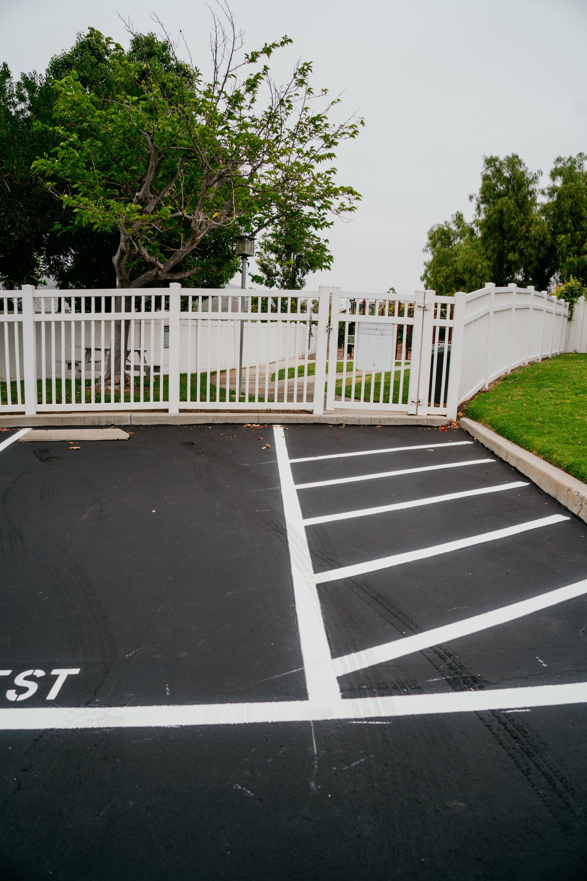 A white fence surrounds a parking lot with the word exit painted on it