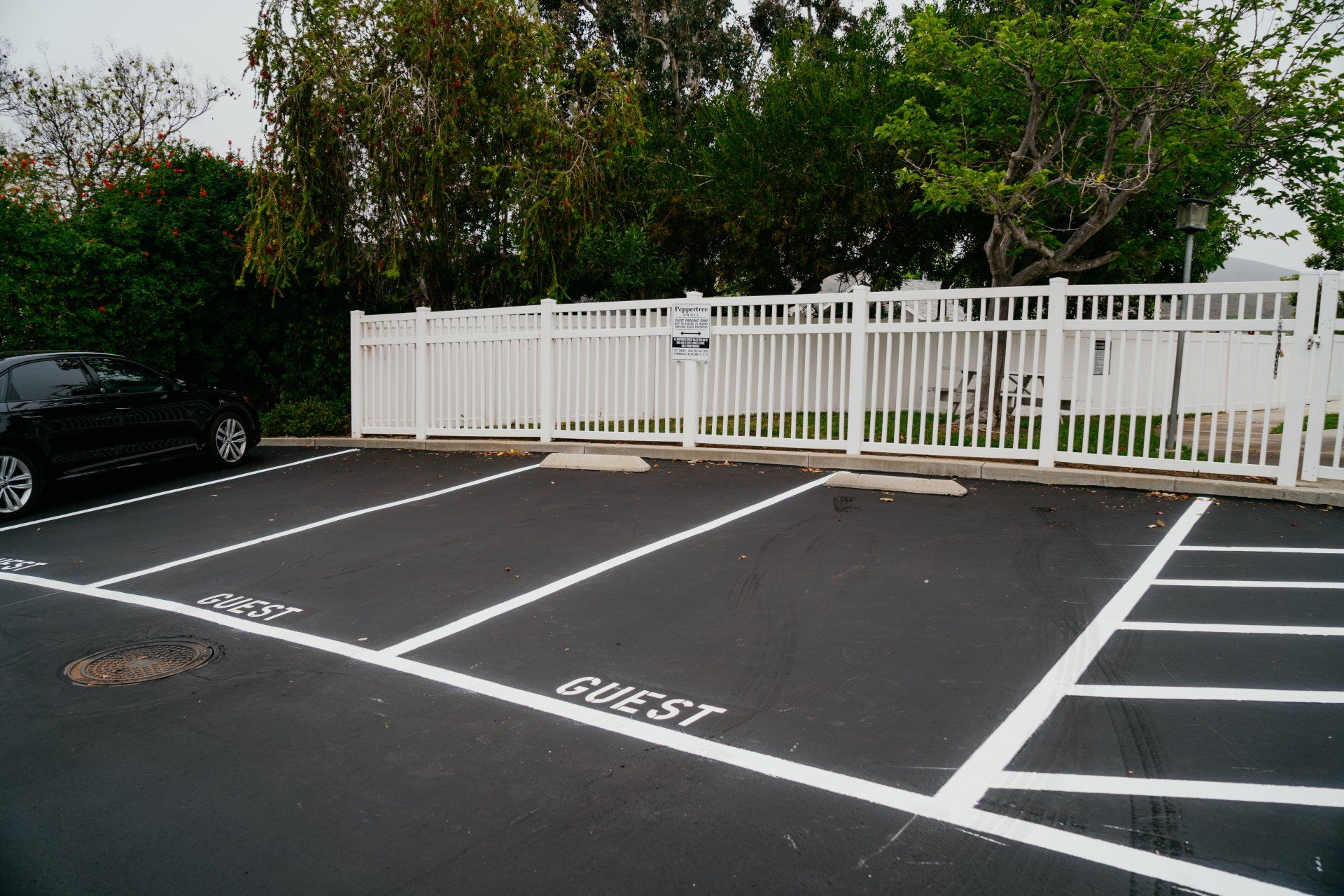 A black car is parked in a parking lot next to a white fence