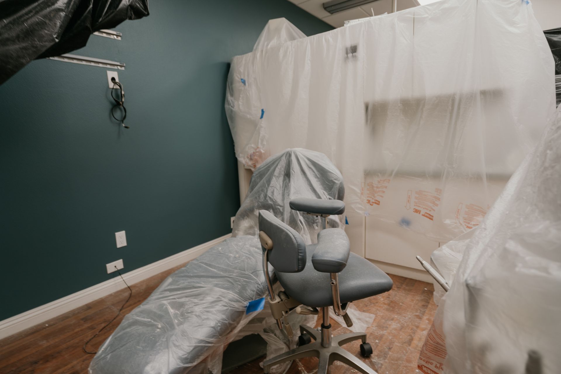 A dental chair is sitting in a room covered in plastic.