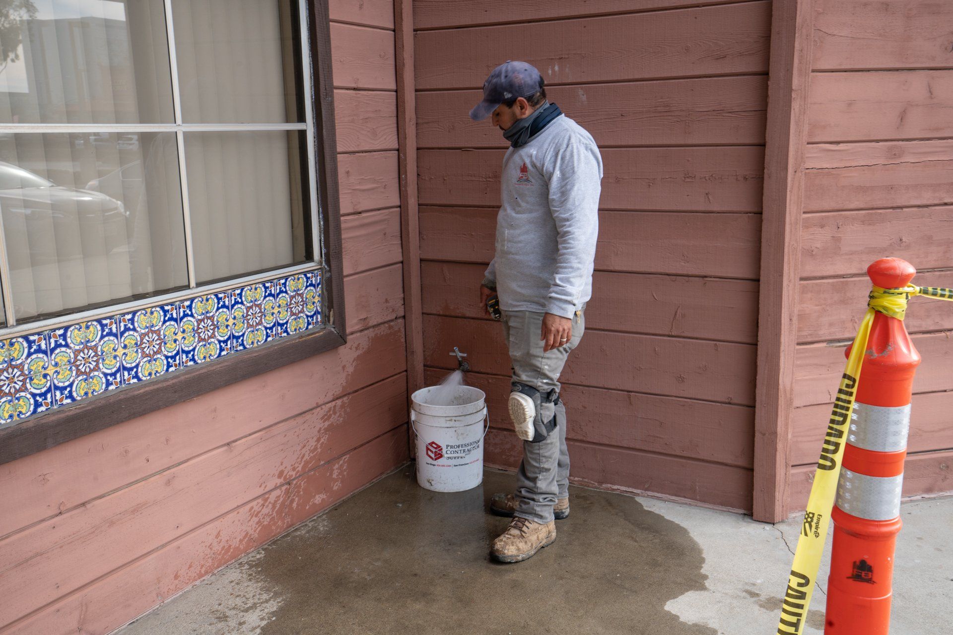 A man is standing in front of a building with a bucket in his hand.