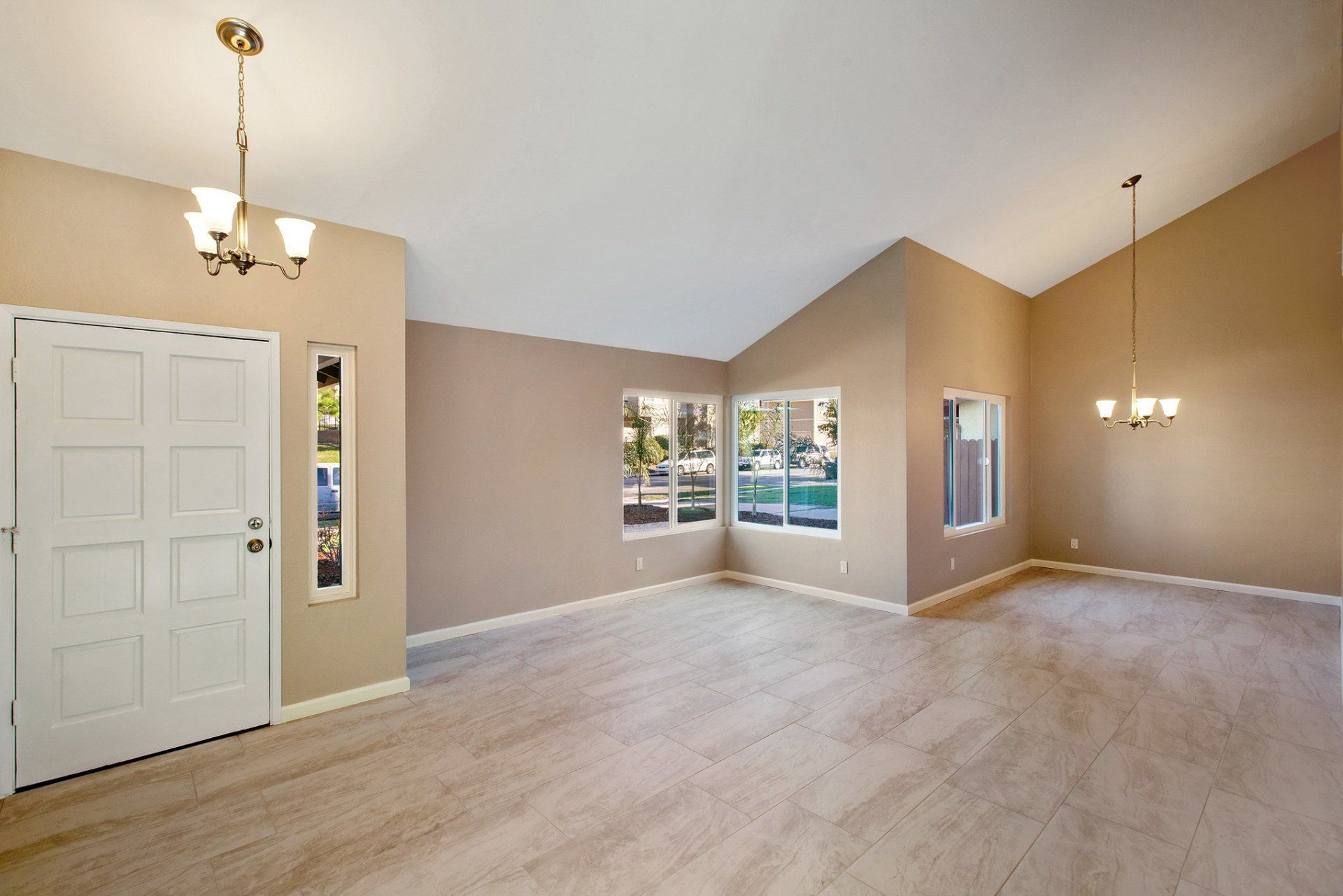 An empty living room with a vaulted ceiling and a chandelier