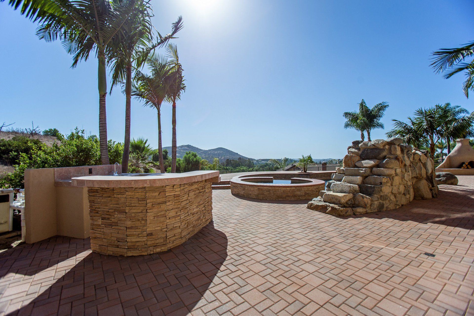 A brick patio with a waterfall and palm trees in the background.