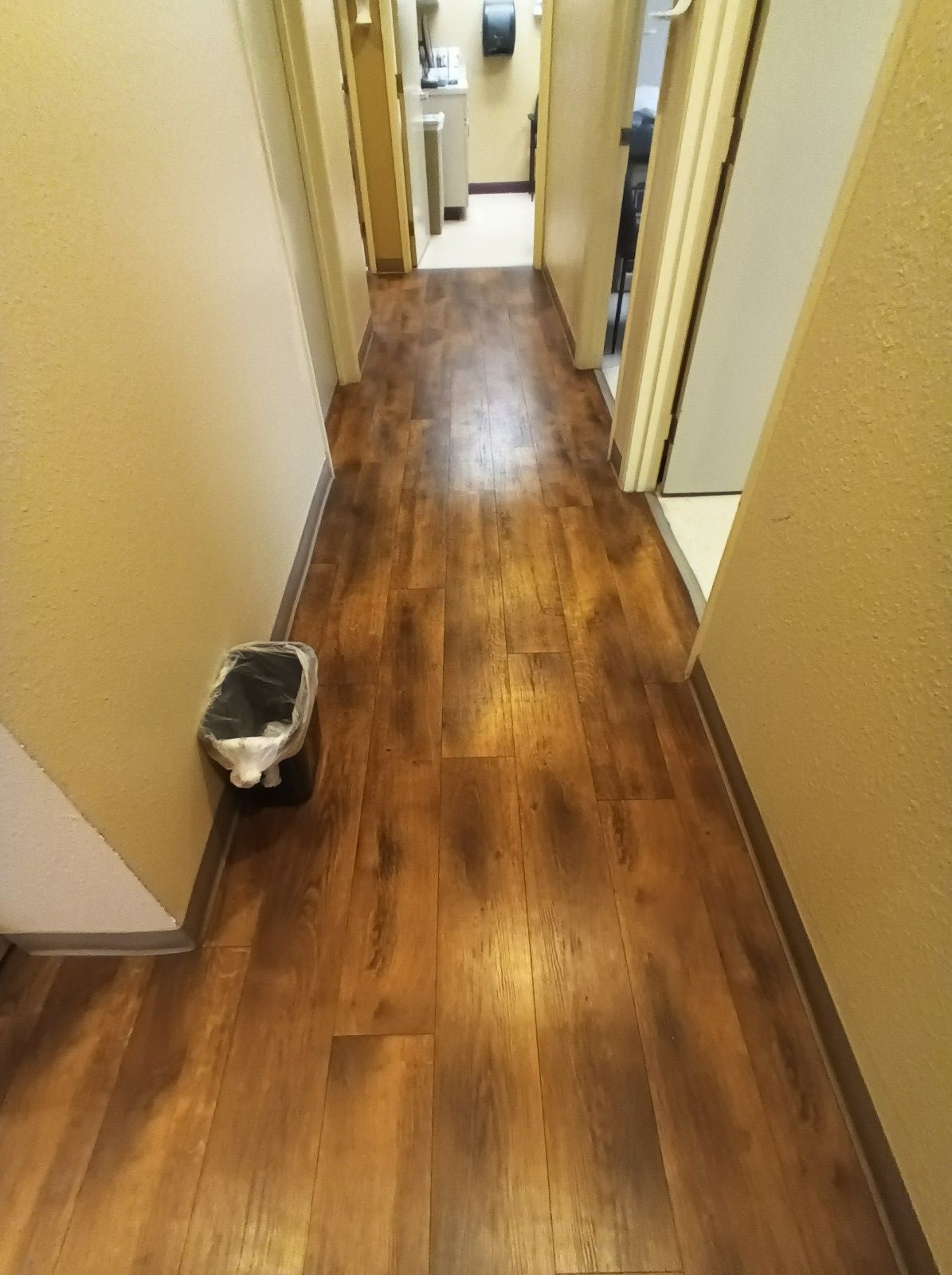 A long hallway with wooden floors and a trash can on the side.
