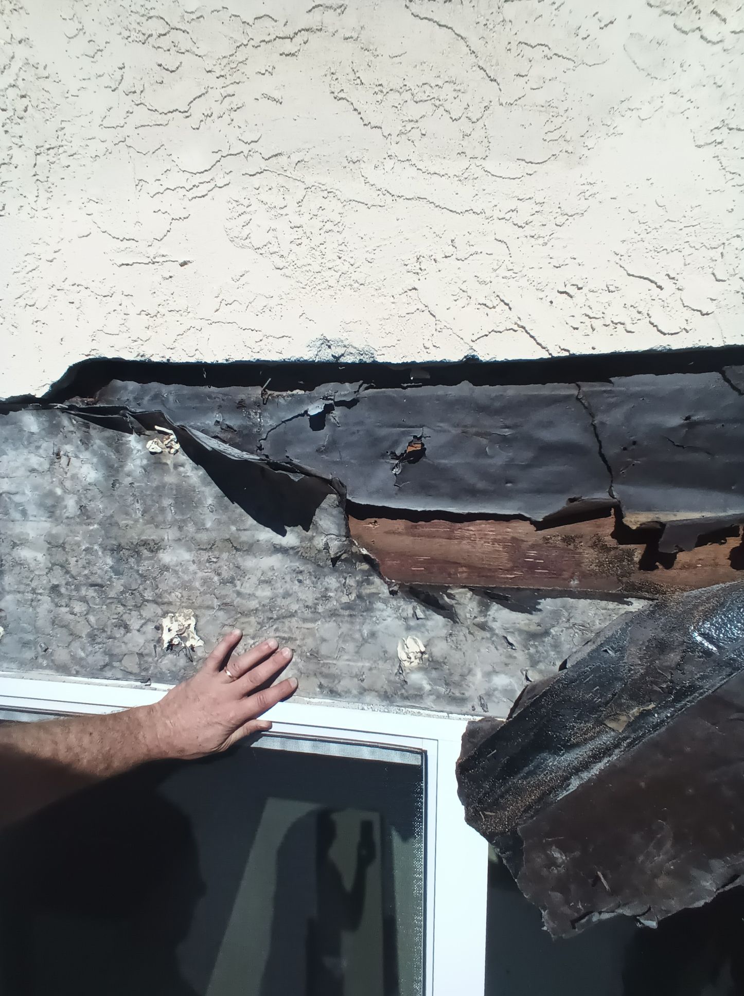 A man 's hand is reaching for a piece of roof that is missing
