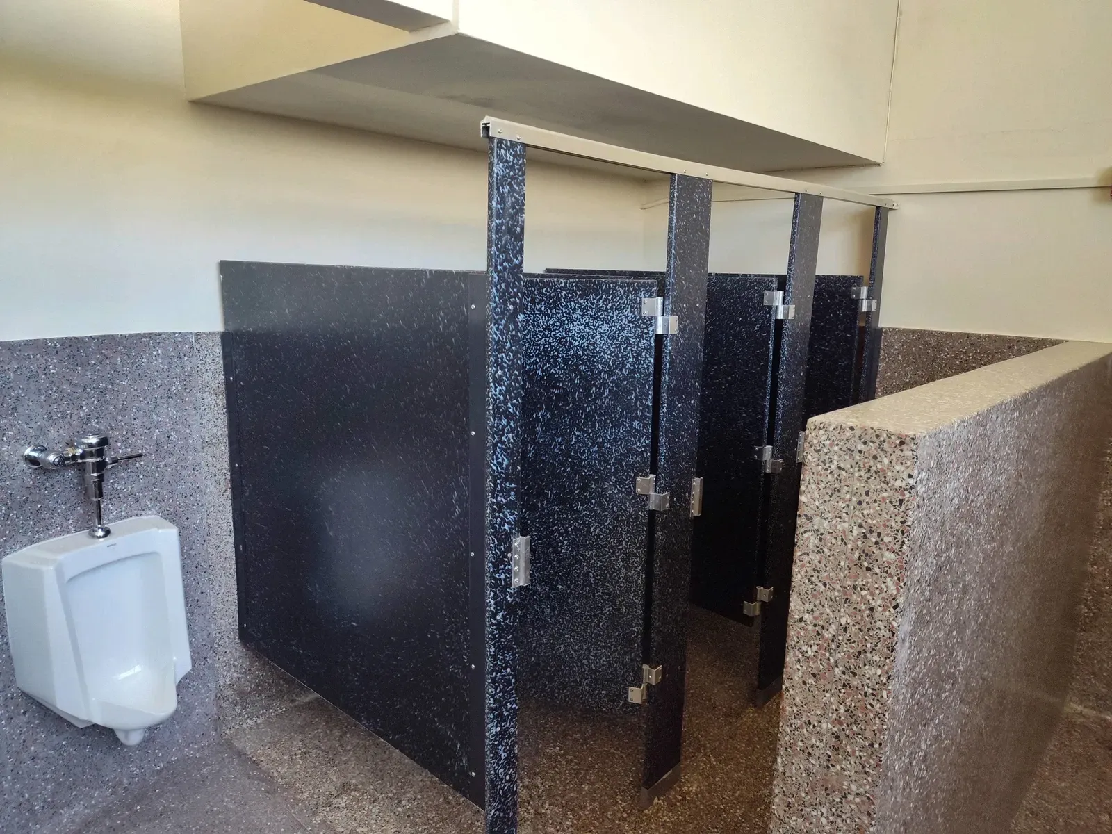 A bathroom with a urinal and a row of stalls