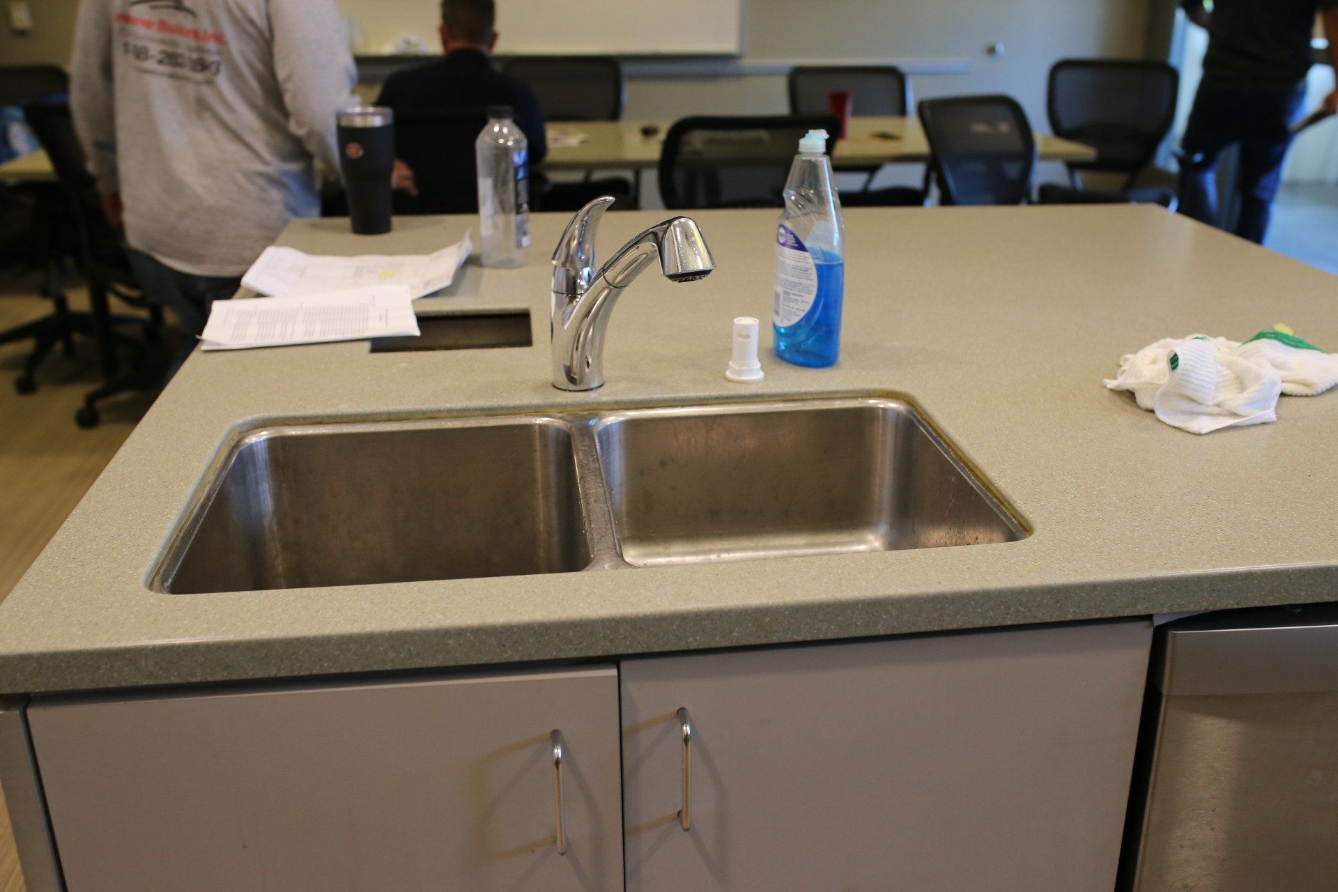 A kitchen sink with a bottle of hand soap on the counter