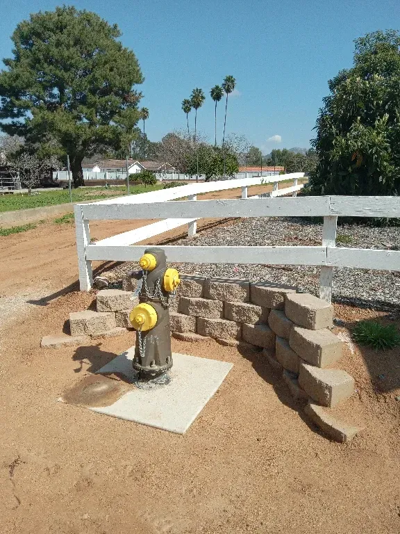 A fire hydrant is sitting in the dirt next to a white fence.