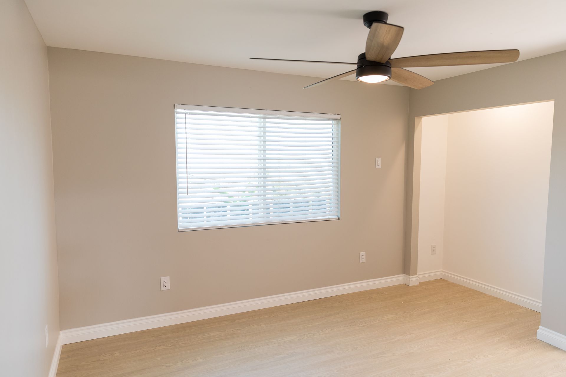 An empty living room with a ceiling fan and a window.