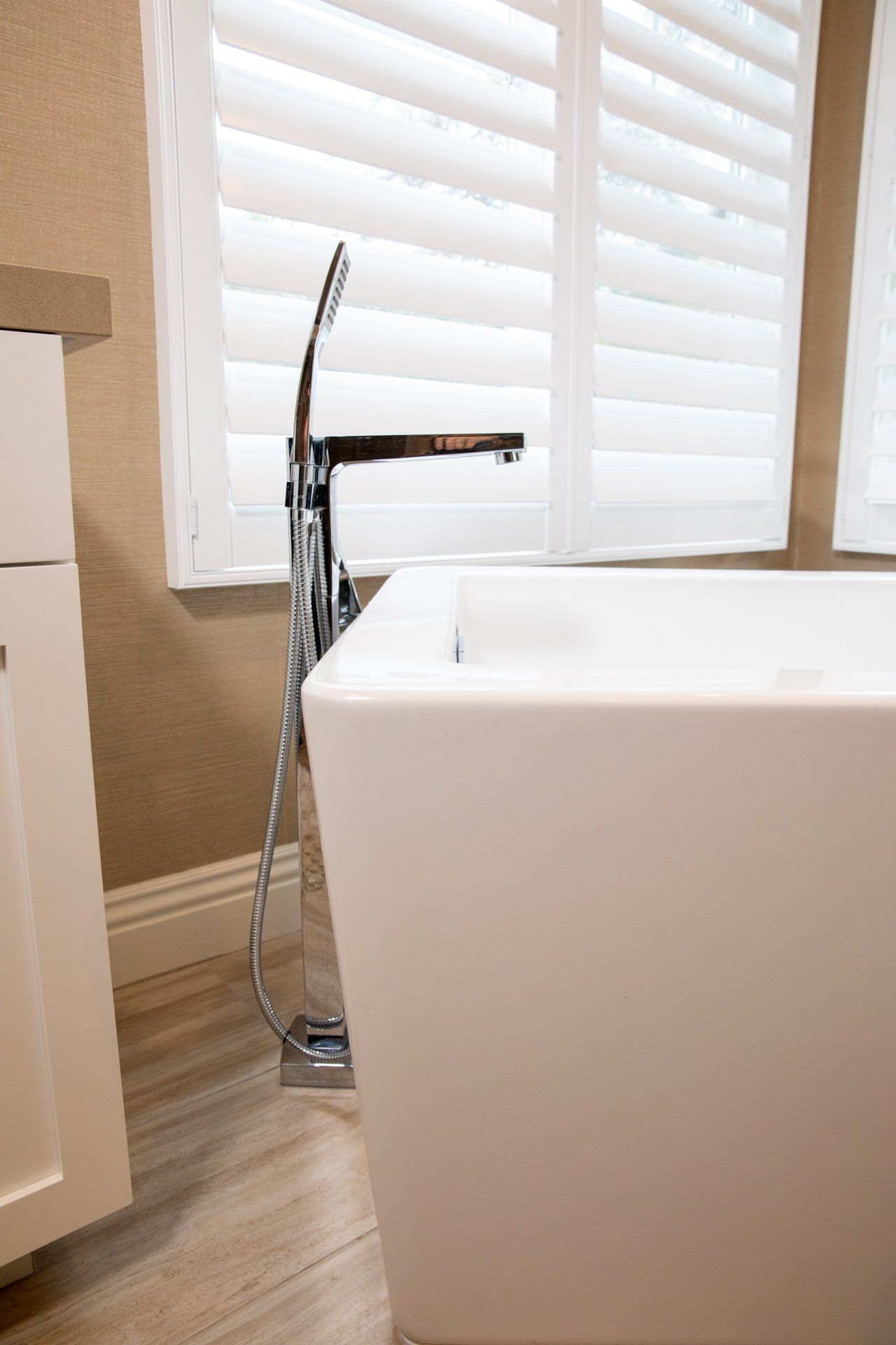 A bathtub in a bathroom next to a window with shutters